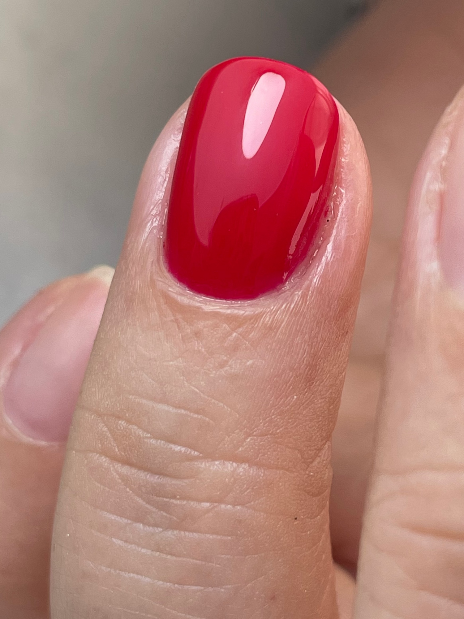 Close-up of a finger with red gel polish and builder gel on. On a neutral background