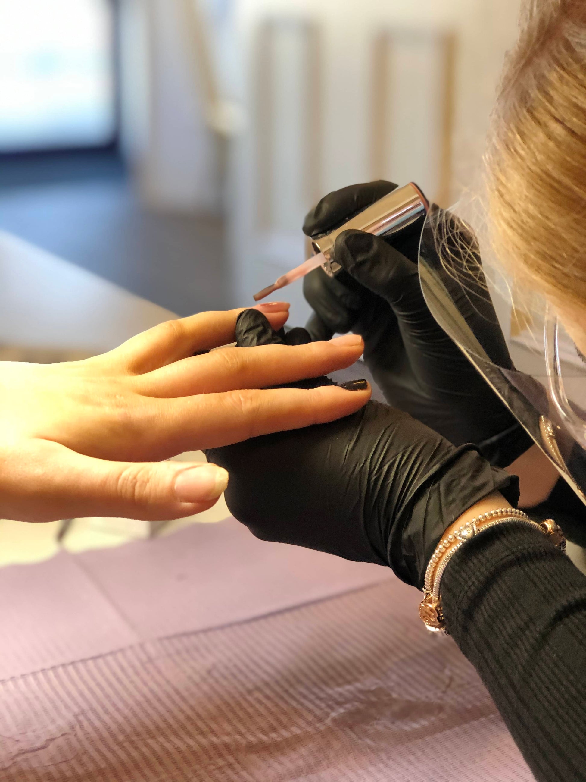 Student applying builder in a bottle to a clients nail in a nail technicians course